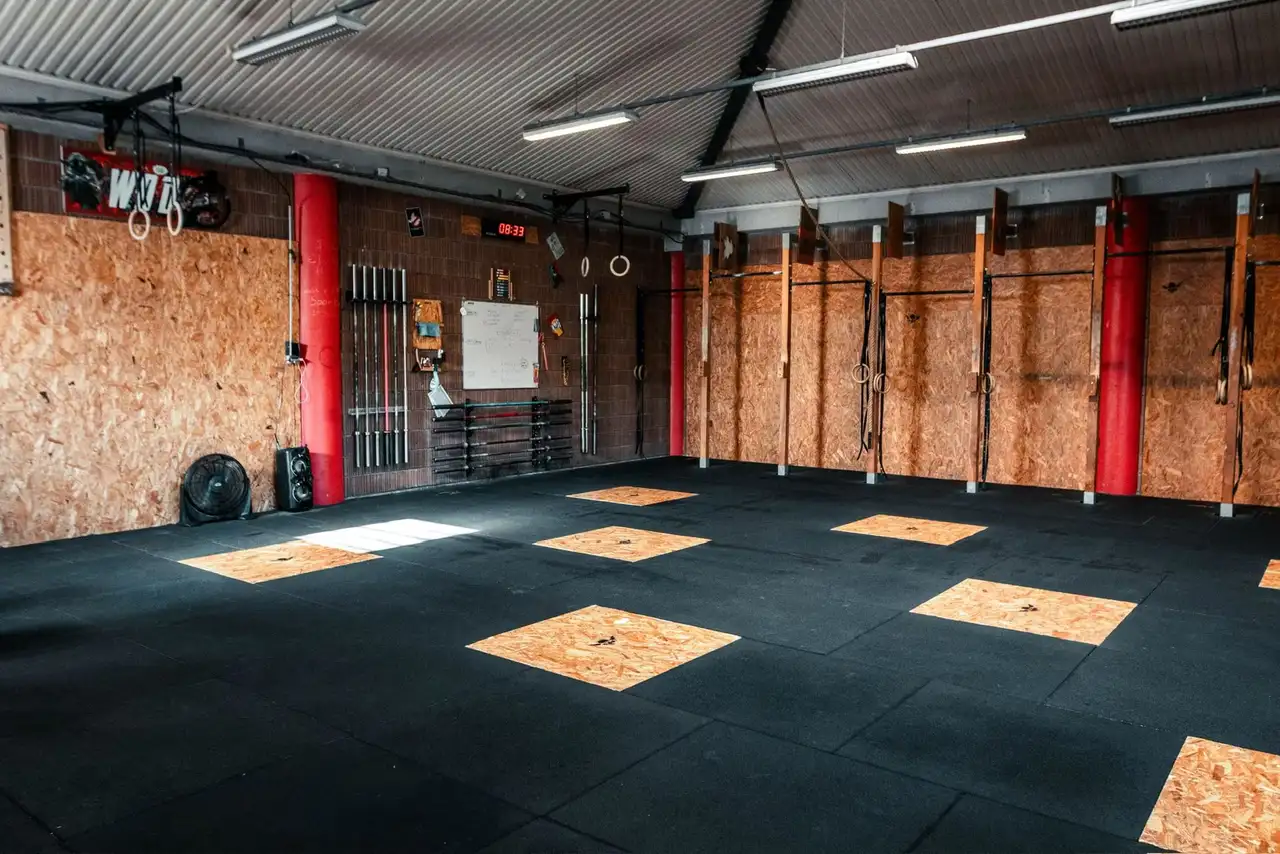 La surface d'entraînement de la box : sol caoutchouc noir, carrés d'OSB, poteaux rouges et rig au fond.